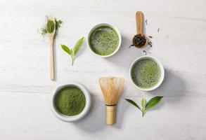 biologisch matcha groen thee poeder in kom met draad vliegenmepper en groen thee blad Aan wit steen tafel, biologisch Product van de natuur voor gezond met traditioneel stijl foto