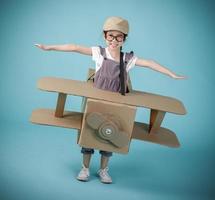 Aziatisch weinig kind meisje spelen met karton speelgoed- vliegtuig handwerk geïsoleerd Aan blauw achtergrond, creatief Bij huis en dromen van vlucht concept foto