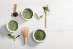 biologisch matcha groen thee poeder in kom met draad vliegenmepper en groen thee blad Aan wit steen tafel, biologisch Product van de natuur voor gezond met traditioneel stijl foto