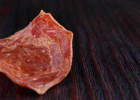 vlees chips. een single stuk van droog vlees leugens Aan een donker houten oppervlak. foto