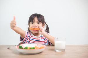 schattig Aziatisch kind meisje aan het eten gezond groenten en melk voor haar maaltijd foto
