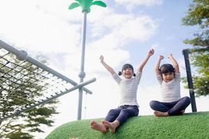 kind spelen op buitenspeeltuin. kinderen spelen op school of kleuterschool. actieve jongen op kleurrijke glijbaan en schommel. gezonde zomeractiviteit voor kinderen. klein meisje buitenshuis klimmen. foto