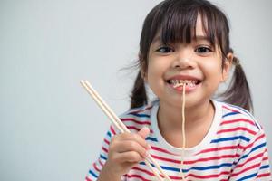 schattig Aziatisch kind meisje aan het eten heerlijk ogenblik noedels Bij huis. foto