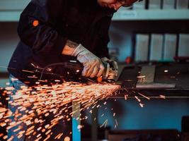 zware industrie engineering fabrieksinterieur met industriële werknemer die haakse slijper gebruikt en een metalen buis snijdt. aannemer in veiligheidsuniform en bouwhelm voor het vervaardigen van metalen constructies. foto