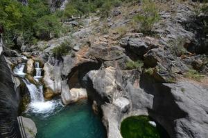 berg waterval in een rotsachtig kloof overwoekerd met groen Woud. stroom van ijzig water valt Aan bemost stenen. foto