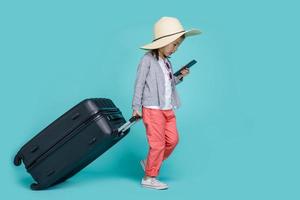 Aziatisch weinig meisje is gebruik makend van een smartphone naar controleren vlucht naar reizen Aan weekenden, leeg ruimte in studio schot geïsoleerd Aan kleurrijk blauw achtergrond foto