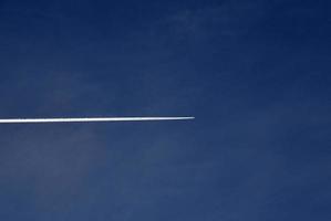 een vlak vliegend in de blauw lucht en wolken. een wit contrail van een vliegtuig in de zomer lucht. foto