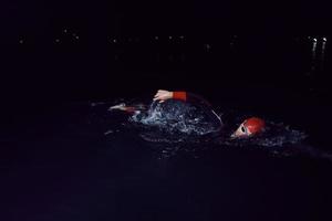 triatlonatleet die in donkere nacht zwemt die wetsuit draagt foto