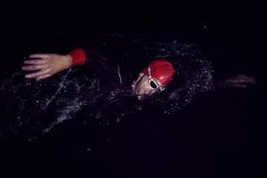 triatlonatleet die in donkere nacht zwemt die wetsuit draagt foto