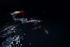 triatlonatleet die in donkere nacht zwemt die wetsuit draagt foto