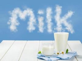 twee glas van melk met tafellinnen Aan een wit houten tafel Aan een blauw lucht achtergrond, lekker, voedzaam en gezond zuivel producten foto