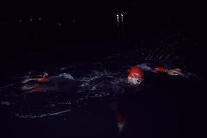 triatlonatleet die in donkere nacht zwemt die wetsuit draagt foto