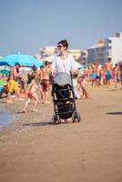 moeder wandelen Aan strand en Duwen baby vervoer foto