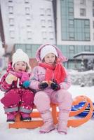 portret van twee weinig meisjes zittend samen Aan sleeën foto