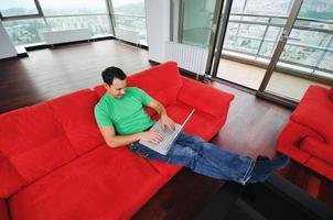 Mens ontspannende Aan sofa en werk Aan laptop computer foto