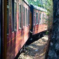 speelgoedtrein die zich op berghellingen beweegt, prachtig uitzicht, een zijberg, een zijvallei die zich op een spoorlijn naar de heuvel beweegt, tussen groen natuurlijk bos. speelgoedtrein van kalka naar shimla in india, indiase trein foto