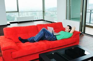 Mens ontspannende Aan sofa en werk Aan laptop computer foto