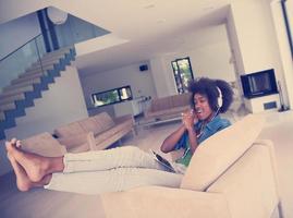 Afrikaanse Amerikaans vrouw Bij huis in stoel met tablet en hoofd telefoons foto