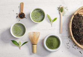 biologisch matcha groen thee poeder in kom met draad vliegenmepper en groen thee blad Aan wit steen tafel, biologisch Product van de natuur voor gezond met traditioneel stijl foto