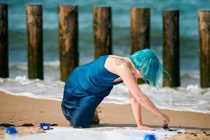 artistieke blauwharige vrouwelijke performancekunstenaar besmeurd met gouacheverf op groot doek op strand foto