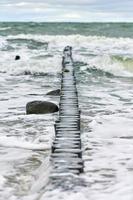 uitzicht op blauwe zee met schuimende golven en houten golfbrekers foto