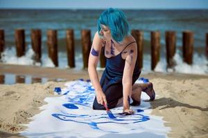 artistieke blauwharige vrouwelijke performancekunstenaar besmeurd met gouacheverf op groot doek op strand foto