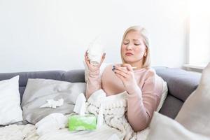 vrouw is hebben griep en ze is gebruik makend van thermometer. ziek met een rhinitis vrouw druipend neus. vrouw wezen ziek hebben griep aan het liegen Aan sofa op zoek Bij temperatuur Aan thermometer, hoog koorts. foto