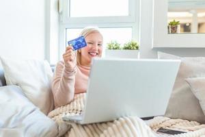 jong vrouw Holding credit kaart en gebruik makend van laptop computer. online boodschappen doen concept. gelukkig vrouw aan het doen online boodschappen doen Bij huis foto