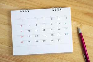 kalenderpagina met pen op houten bureautafel foto