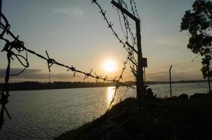 met weerhaken draad hek en een verbazingwekkend silhouet zonsopkomst met achtergrond bergen en reservoir in malang, Indonesië foto