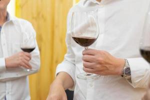dichtbij omhoog naar de handen van twee wit overhemd zakenman houden wijn glas, praten en onderhandelen in bedrijf en politiek kwestie Bij de avondeten feest. foto
