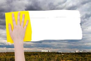 hand- verwijdert regenachtig wolken over- stad- door geel vod foto