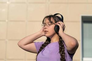 een tiener meisje staat Aan de straat, persen hoofdtelefoons naar haar oren met haar handen en luistert naar muziek- met haar ogen Gesloten. foto