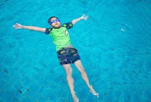 jongen vervelend een zwempak en bril zwemmen in de midden- van de zwembad met een blauw water achtergrond foto