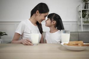 gezond Aziatisch Thais familie, gelukkig weinig dochter, en jong moeder gezicht naar gezicht Bij dining tafel met vers melk in glas en brood zorg samen, welzijn voeding ontbijt maaltijd, ochtend- levensstijl. foto