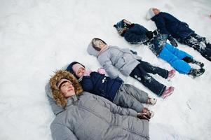 moeder met vier kinderen in de winternatuur die in de sneeuw ligt. foto