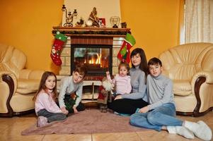 gelukkige jonge grote familie bij een open haard in warme woonkamer op winterdag. moeder met vier kinderen thuis. foto