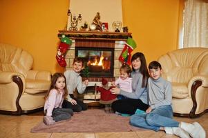 gelukkige jonge grote familie bij een open haard in warme woonkamer op winterdag. moeder met vier kinderen thuis. foto
