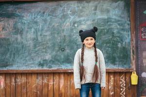 weinig meisje in een hoed poseren Aan de achtergrond van de school- schoolbord foto