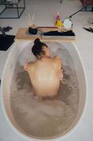 jong vrouw omarmen haarzelf nemen een bad visie van de terug foto