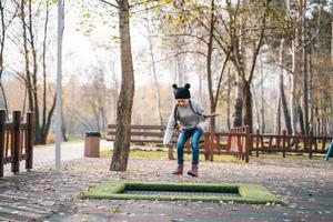 gelukkig school- meisje jumping Aan een klein trampoline in de park foto