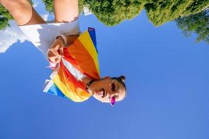 een jong vrouw ontwikkelt een regenboog vlag tegen de lucht foto