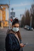 meisje in beschermend masker gebruik makend van smartphone buitenshuis. covid 19. wereld coronavirus pandemie. foto