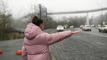 jong vrouw staand Aan weg buitenshuis verhogen hand- terzijde vangen taxi foto