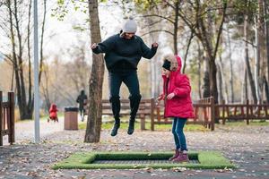 mam en haar dochter jumping samen Aan trampoline in herfst park foto