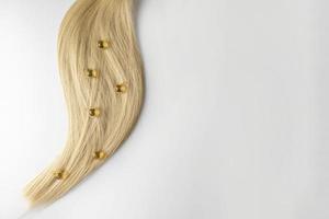 een haar- zorg olie of serum in gouden capsules aan het liegen Aan een strand van blond haar, Product afzet model. een concept van haar- zorg in een salon of Bij huis foto
