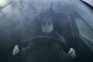 jong vrouw in een masker en handschoenen het rijden een auto. foto