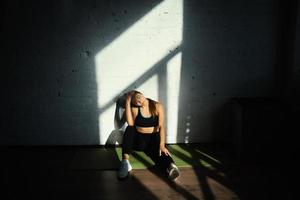 fit vrouw resting na huis training, zittend Aan mat foto