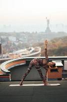 vrouw aan het doen yoga Aan de dak van een wolkenkrabber in groot stad. foto