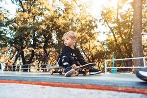 jong kind zittend in de park Aan een skateboard. foto